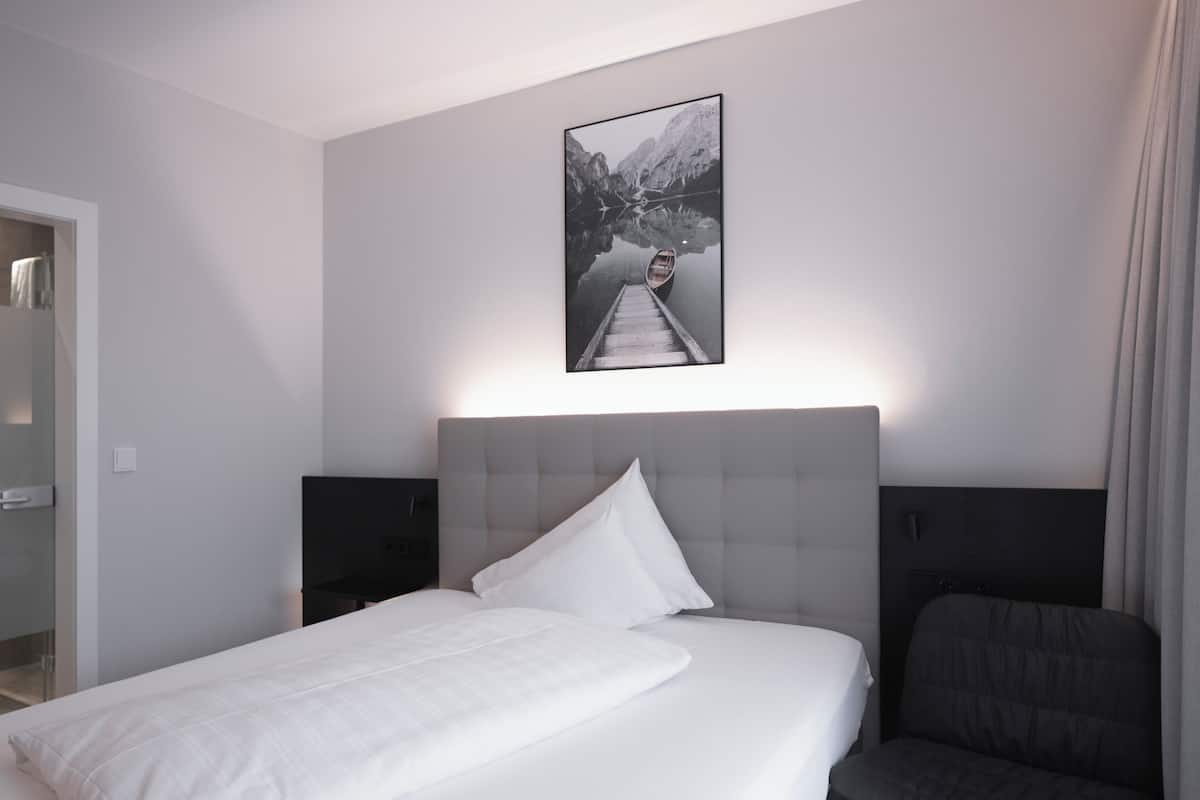 A modern hotel room with a large bed, a headboard, a flat-screen TV, and a framed picture of a mountain lake.