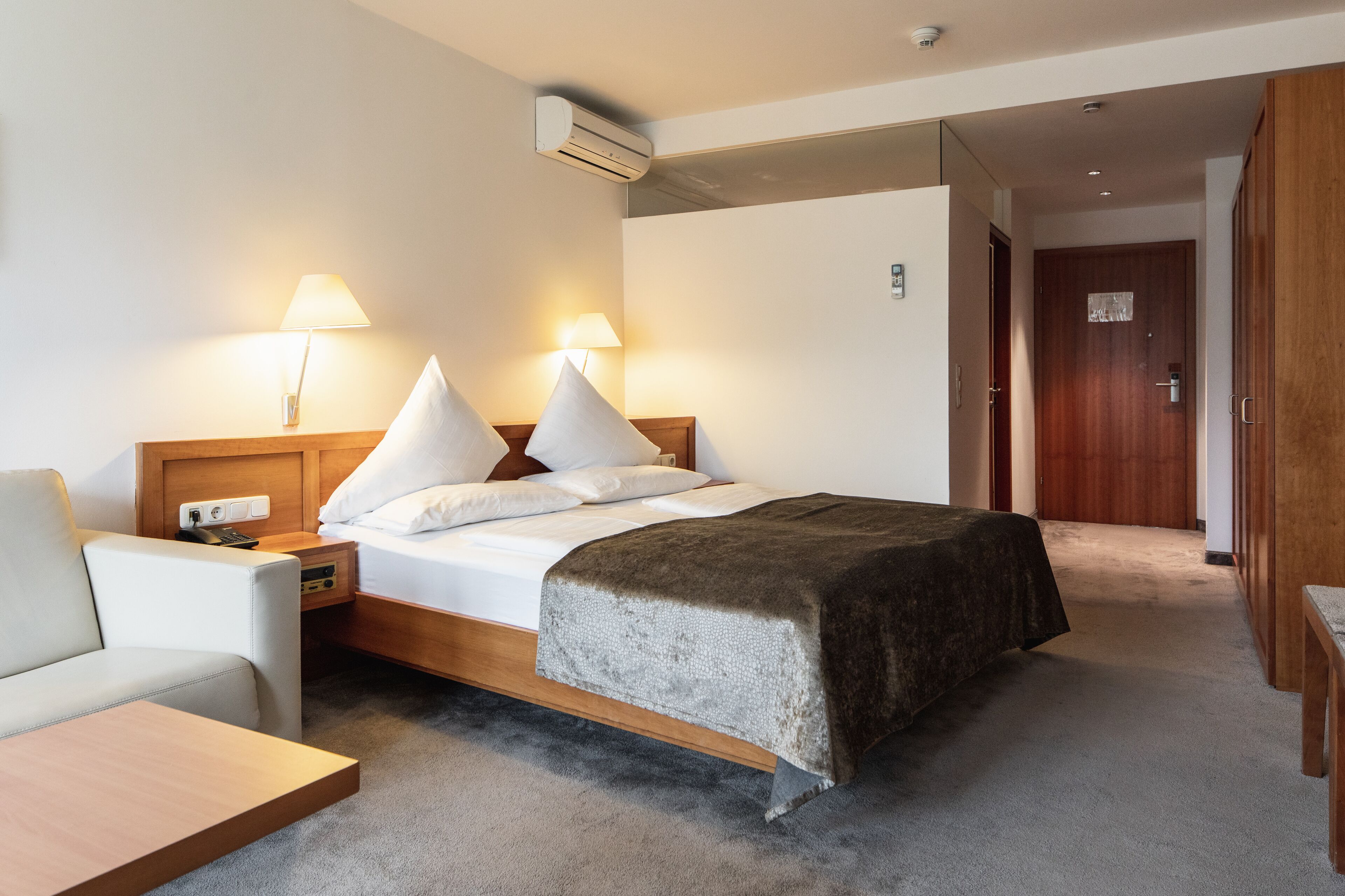 A hotel room with a bed, bedside lamps, a desk, and a chair.