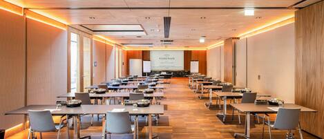 A conference room with multiple tables and chairs, a projector screen, and a presentation area.