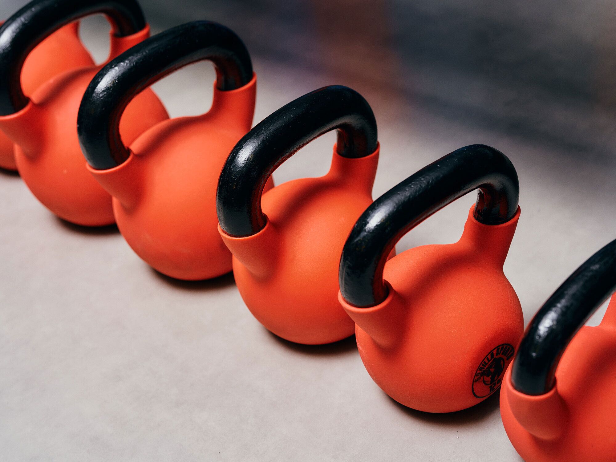 A row of orange kettlebells with black handles.