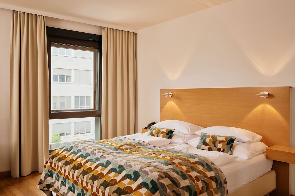 A hotel room with a large bed, a wooden headboard, and a window with curtains.