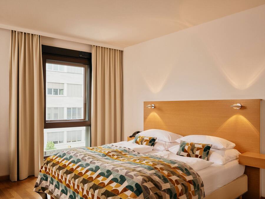 A hotel room with a large bed, a wooden headboard, and a window with curtains.