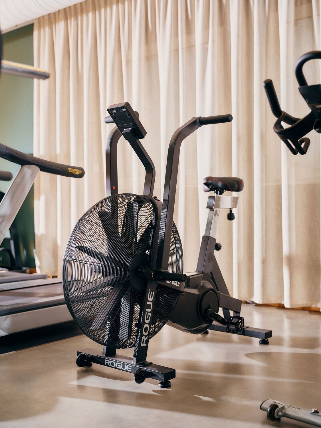 A stationary bike in a room with a treadmill and a fan.