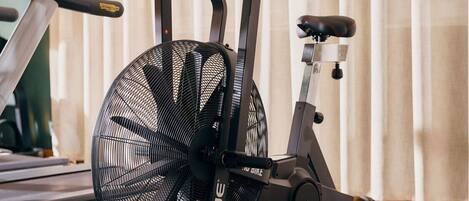 A stationary bike in a room with a treadmill and a fan.
