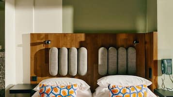 A hotel room with a wooden headboard, two beds with white linens, and colorful patterned pillows.