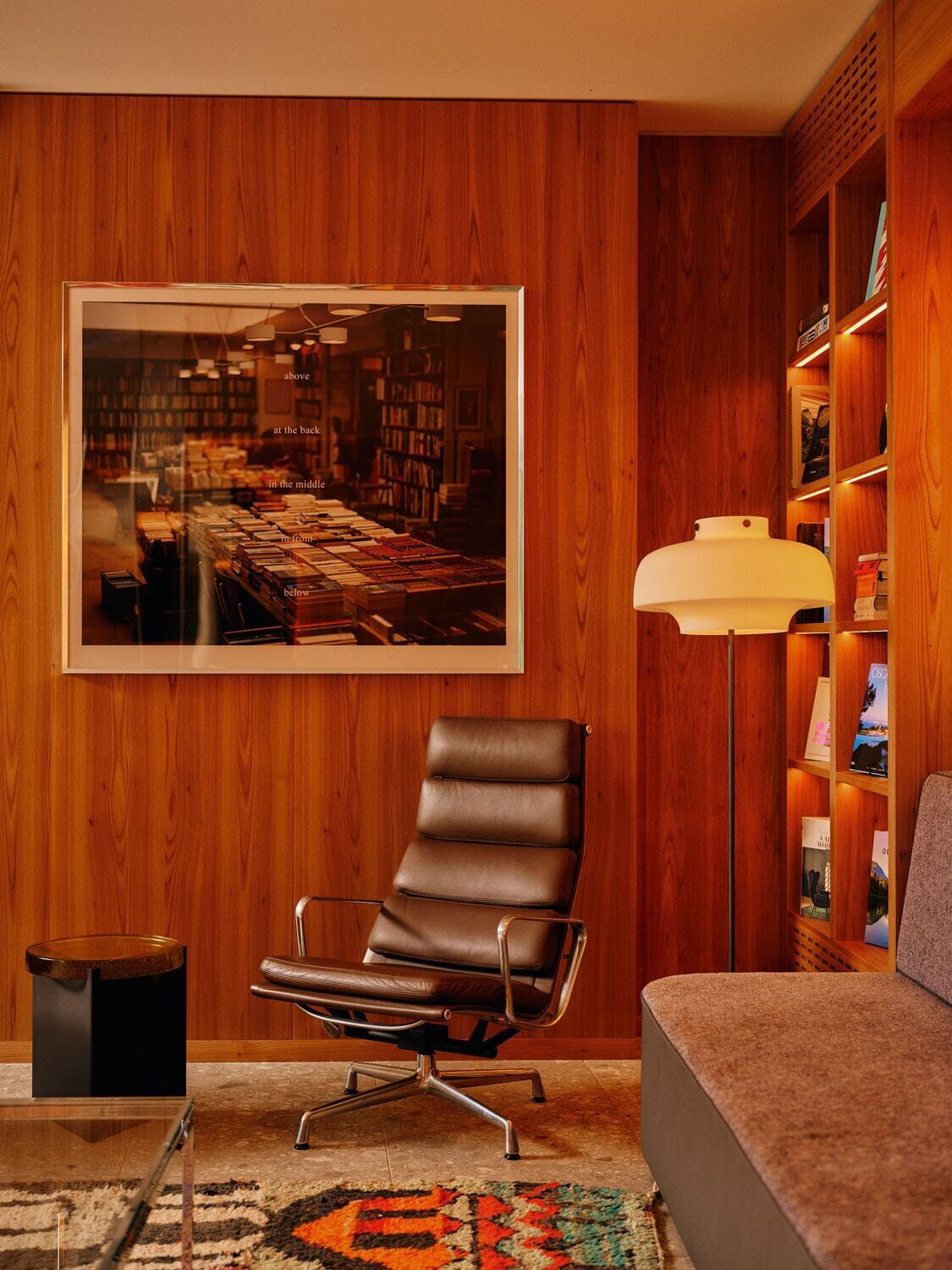A modern living room with a leather chair, a sofa, a floor lamp, and a bookshelf.