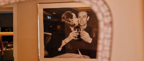 A framed photograph of a couple holding glasses, mounted on a wall in a room with a red couch.
