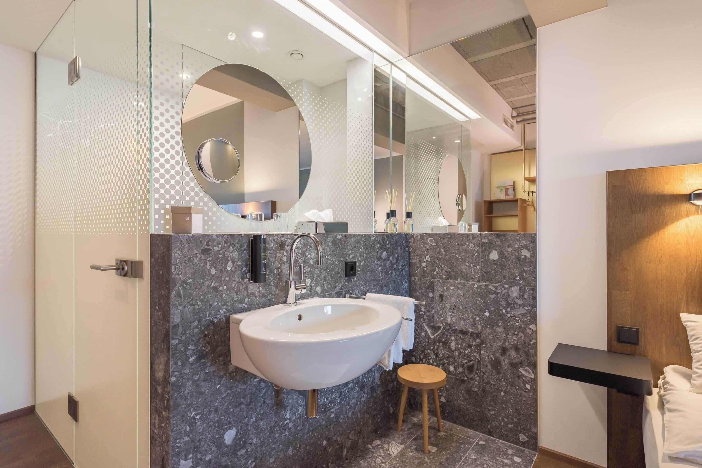 Un baño moderno con un lavamanos grande, un espejo y un taburete de madera.