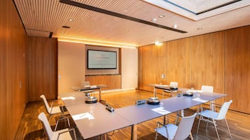 Une salle de conférence avec une longue table, des chaises, un écran de projection et des panneaux de bois.