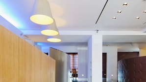 Un moderno vestíbulo de hotel con un mostrador de recepción de madera, un área de descanso y una pared curva con respaldo acolchado.