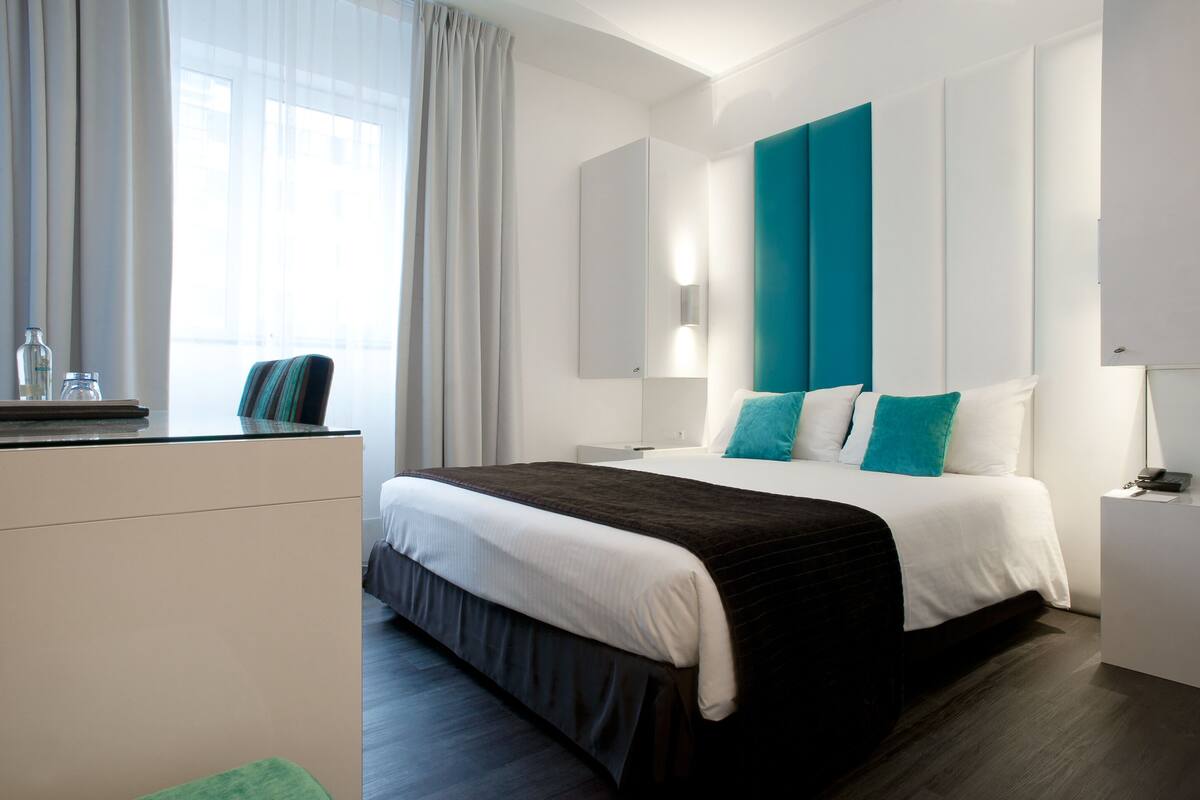 Habitación de hotel moderna con una cama grande, un escritorio y una ventana con cortinas.