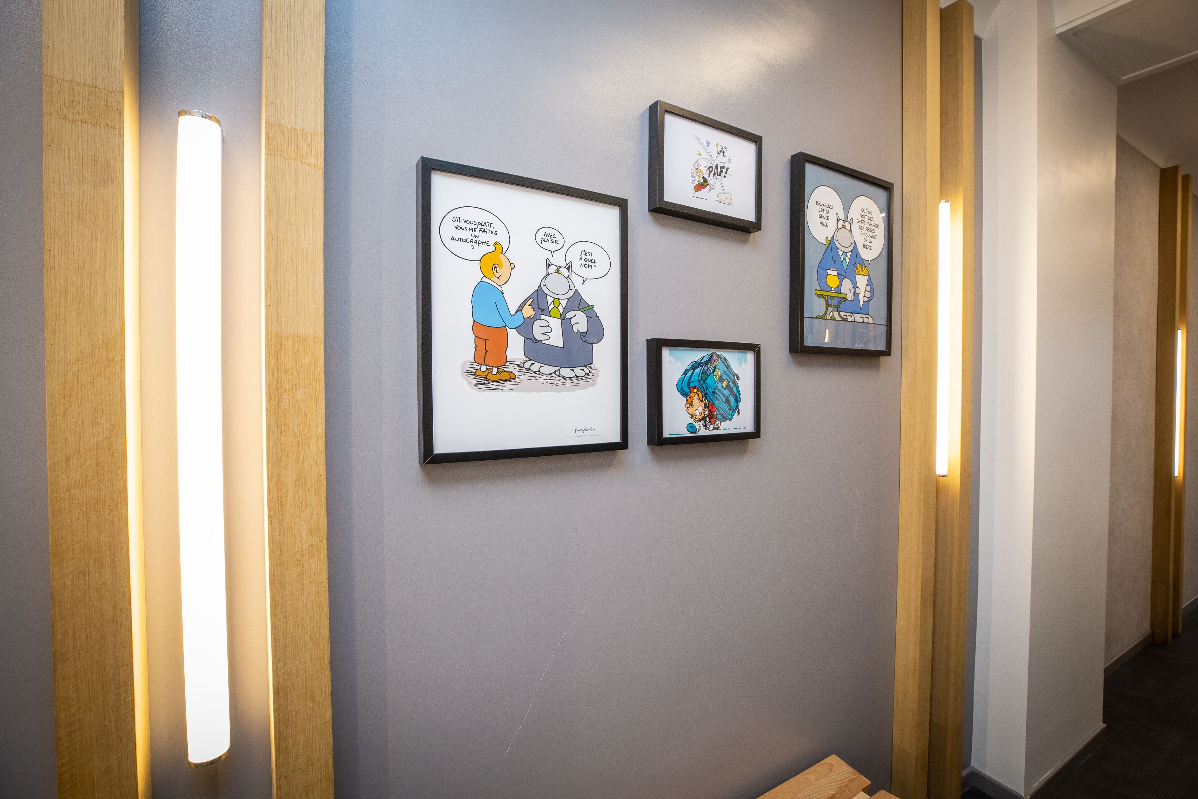 A hallway with framed comic strips on the wall and illuminated vertical light fixtures.