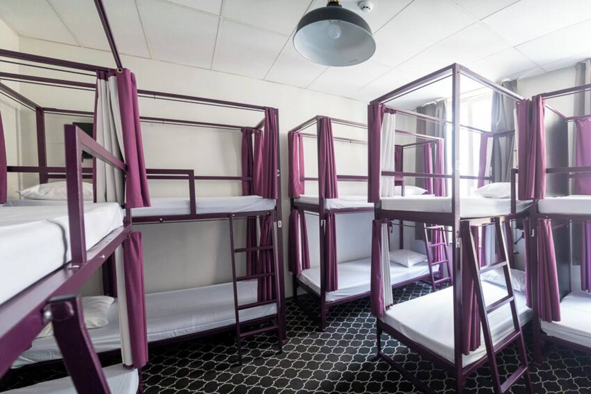 A dormitory room with bunk beds, a window with curtains, and a patterned floor.