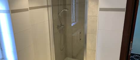 Ducha con mampara de vidrio, pared de azulejos blancos y ventana.