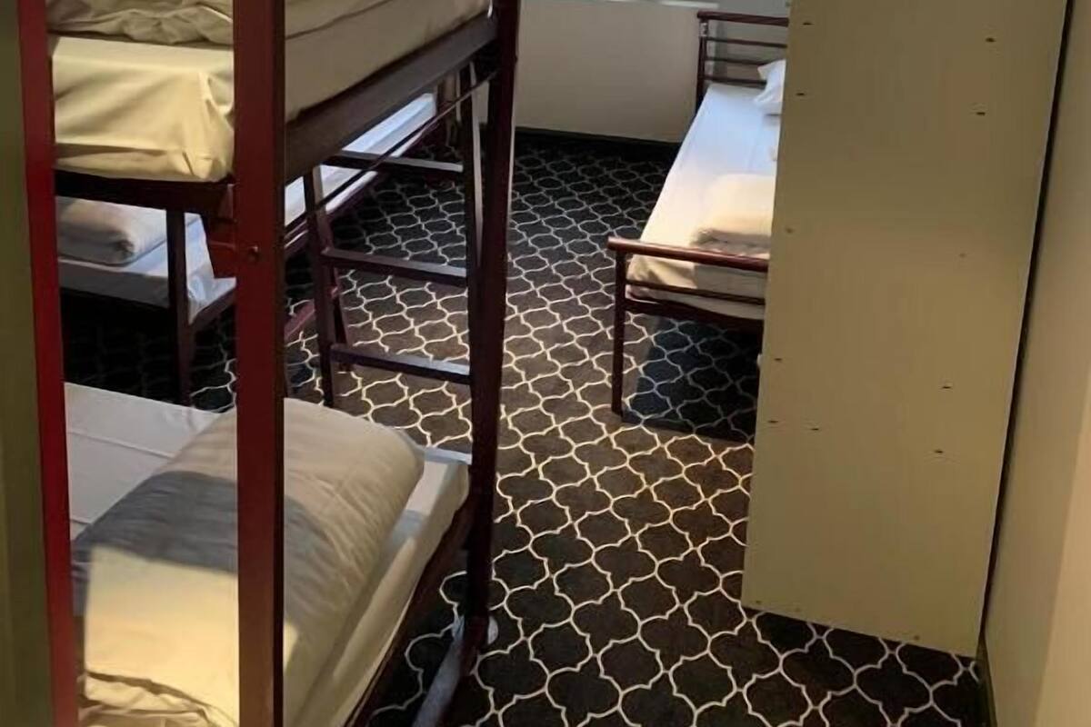 A dormitory room with bunk beds, a window with curtains, and a patterned floor.