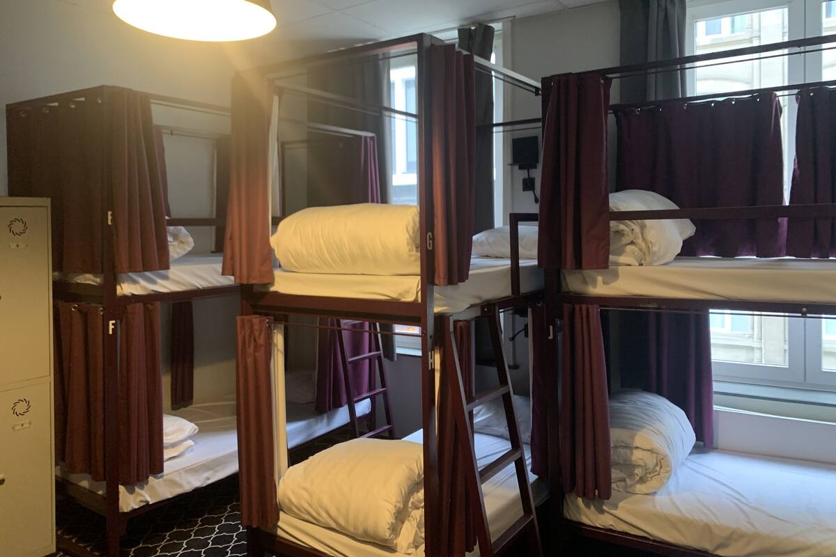 A dormitory room with bunk beds, a desk, and a window with curtains.