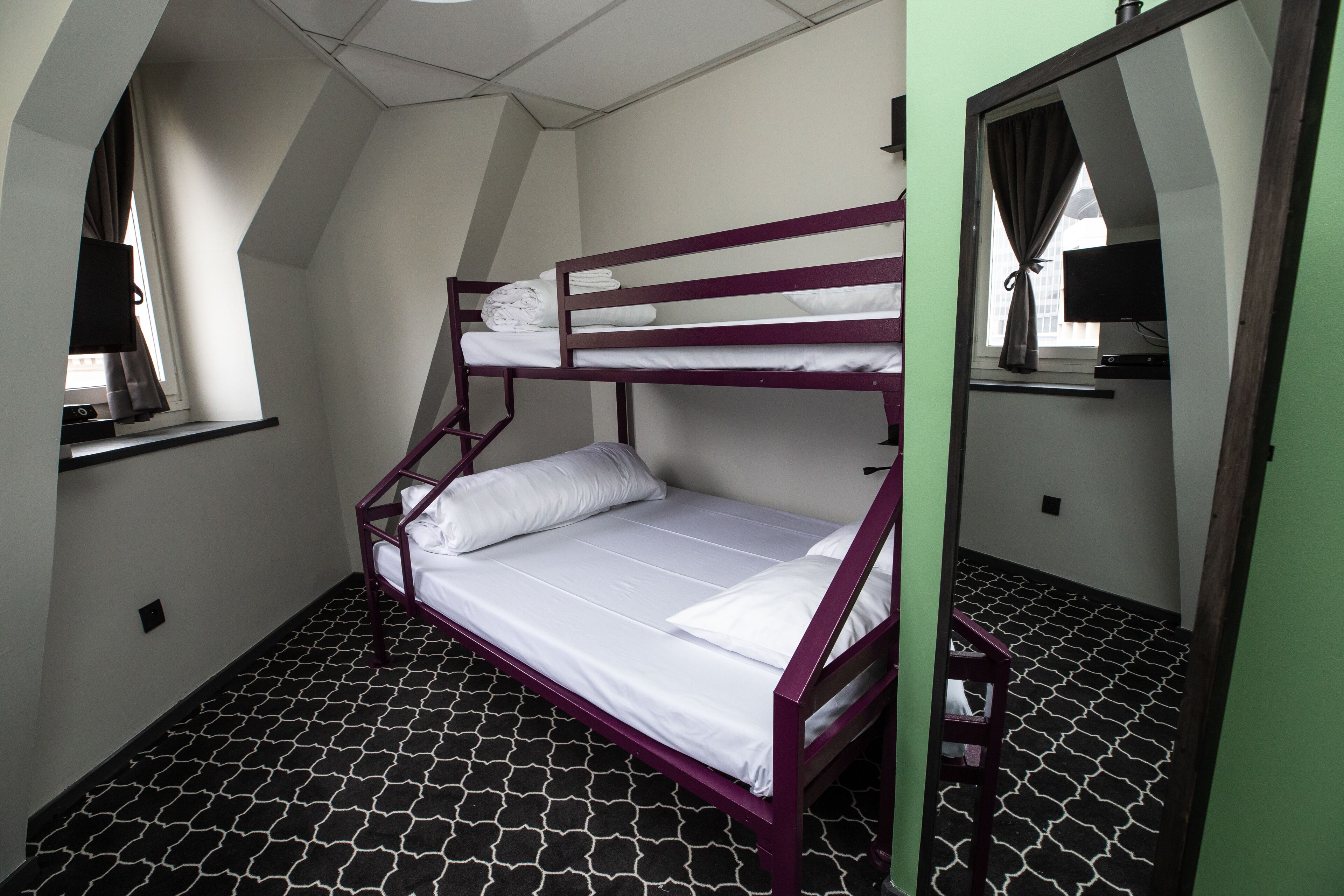 A bunk bed room with a patterned floor, a window with curtains, and a mirror on the wall.