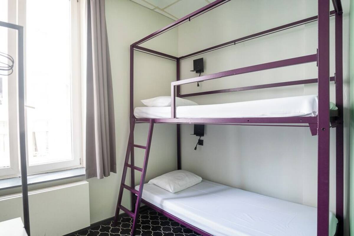 A bunk bed room with a ladder, a window with curtains, and a black and white patterned floor.