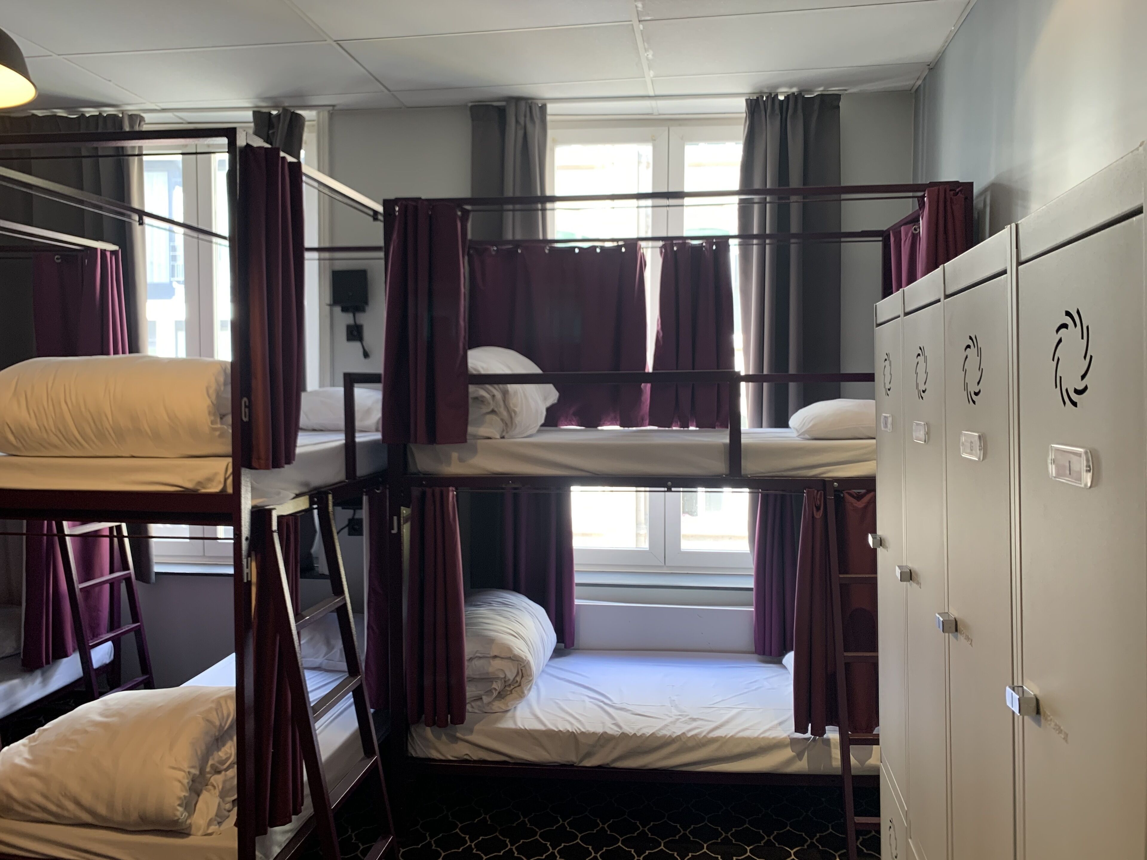 A bunk room with three bunk beds, a wardrobe with circular handles, and a window with curtains.