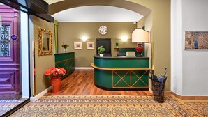 A reception area with a green reception desk, a clock, framed pictures, and a potted plant. - Hotel Mala Strana (Prague)