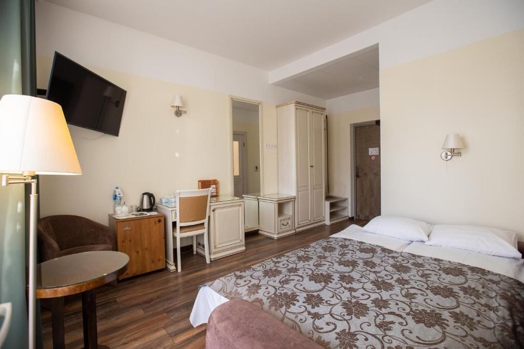 Una habitación de hotel con una cama, un escritorio con una silla, un televisor montado en la pared y un armario.