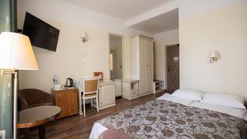 A hotel room with a bed, a desk with a chair, a television mounted on the wall, and a wardrobe.