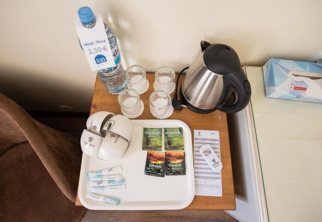 Een dienblad met een waterfles, glazen, een waterkoker, theezakjes en een zak zakdoekjes op een houten tafel.