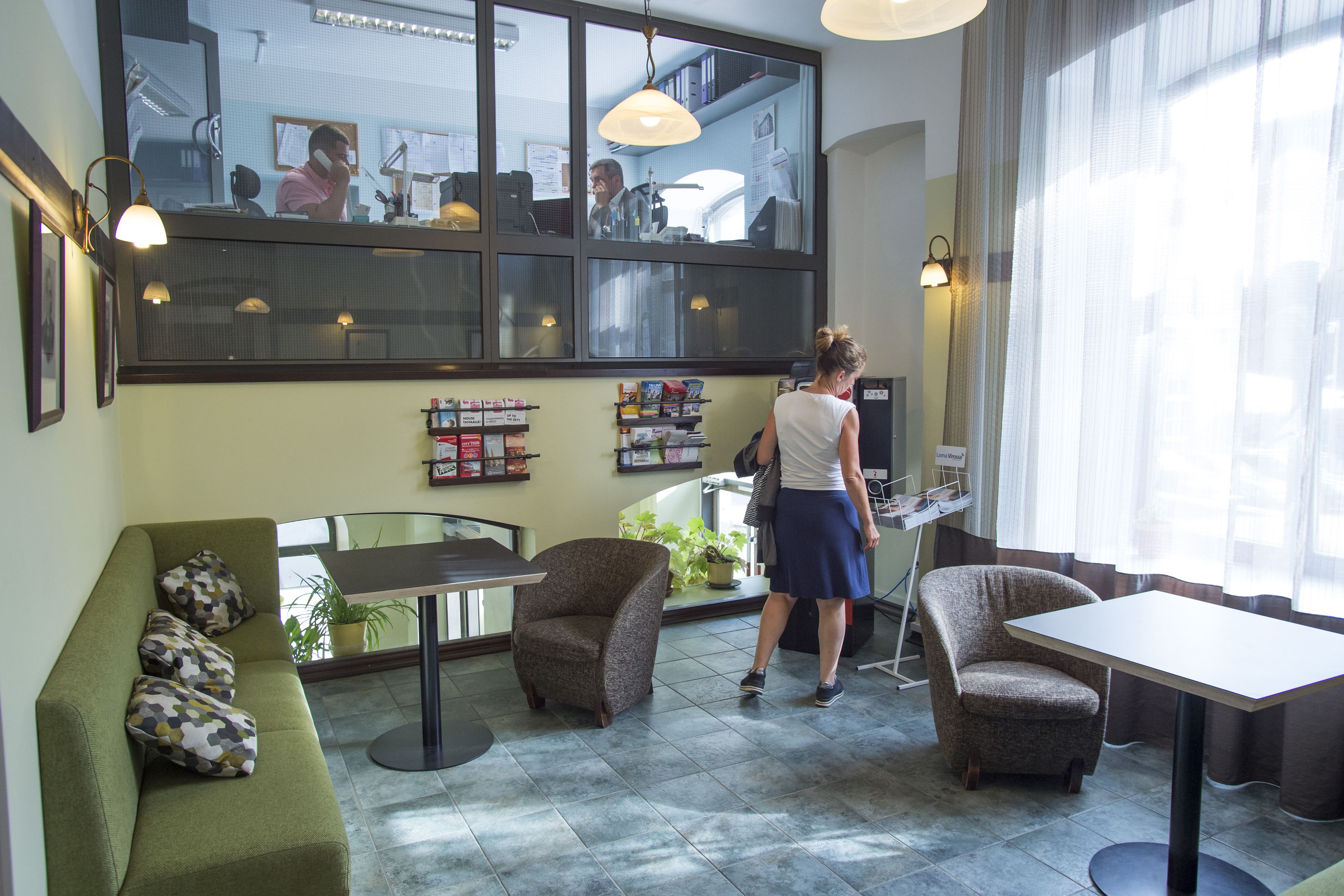 A hotel lobby with a green sofa, two armchairs, a small table, and a reception desk.