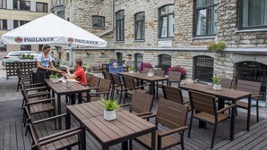 An outdoor dining area with wooden tables and chairs, a white tent with 'PAULANER' branding, and a stone building in the background. - Hotel St. Barbara (Tallinn)