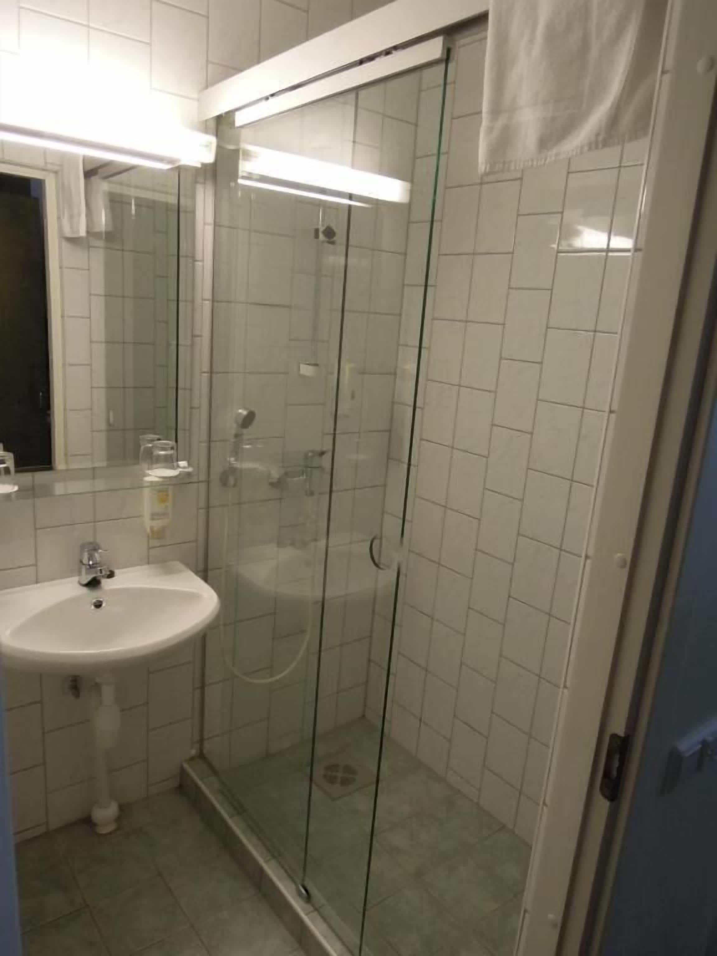 A bathroom with a glass-enclosed shower, a sink, and a mirror.