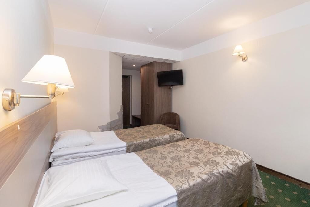 A hotel room with two beds, a flat-screen TV mounted on the wall, a lamp, and a chair.