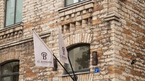 A stone building with a sign for St. Barbara Hotel, featuring a large window, a door with a glass panel, and two potted plants. - Hotel St. Barbara (Tallinn)