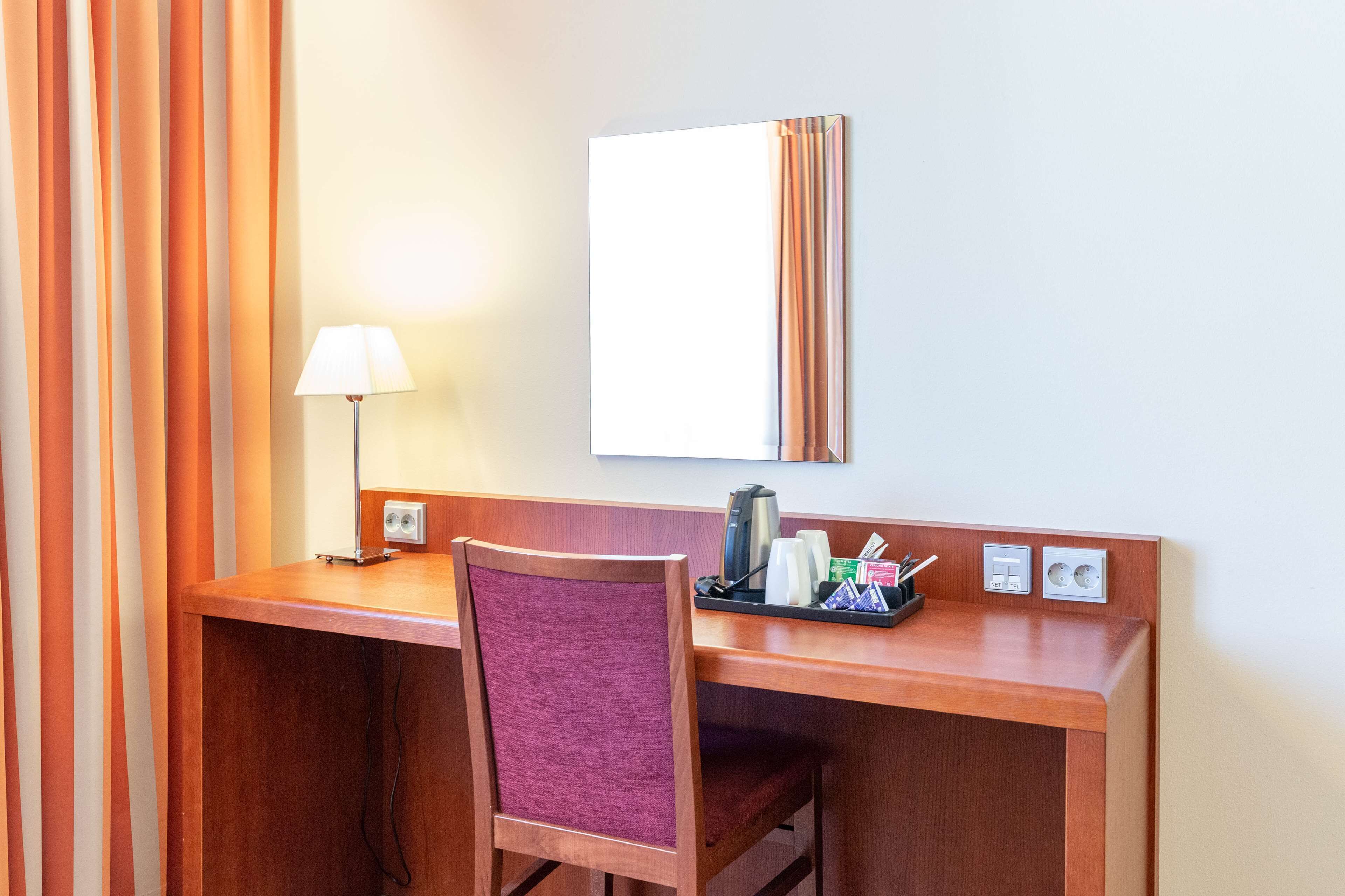 Un bureau dans une chambre d’hôtel, avec une chaise, une lampe, un miroir et un plateau contenant des articles de toilette.
