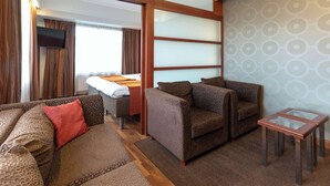 A modern hotel room with a sofa, armchairs, a small table, and a bed with a view. - Scandic Atlas (Kuopio)
