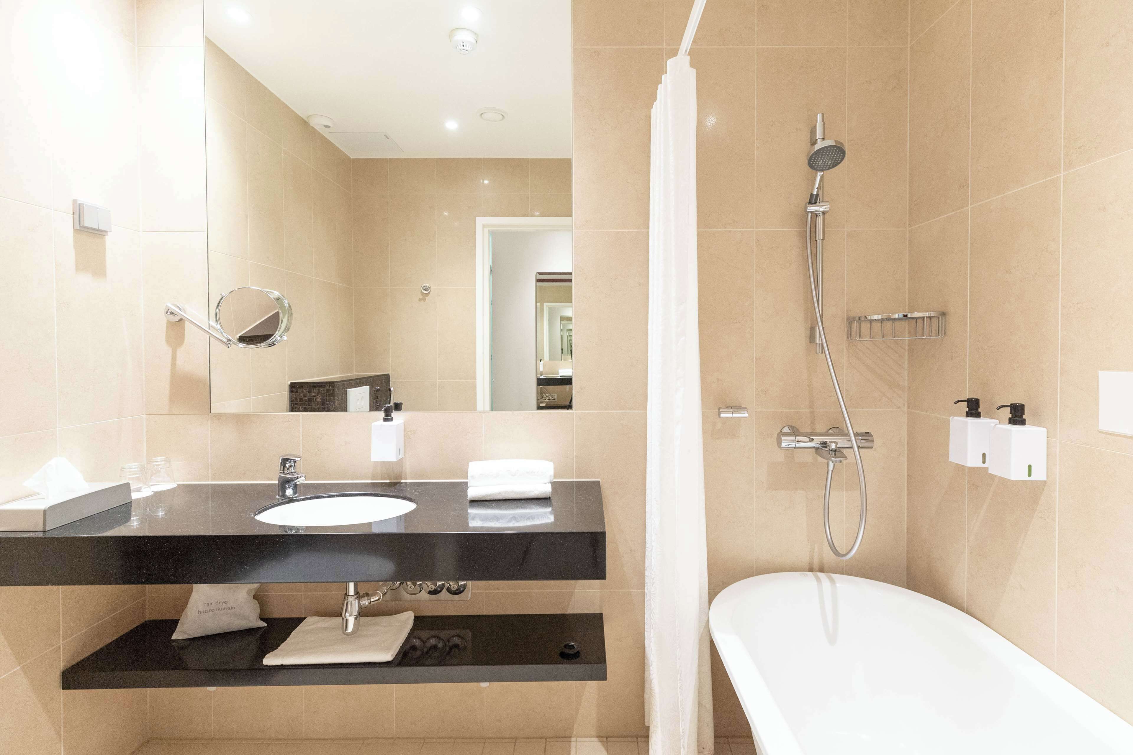 Ein modernes Badezimmer mit einem schwarzen Waschtisch, einem Spiegel, einer weißen Badewanne und einer Dusche mit Duschbrause.