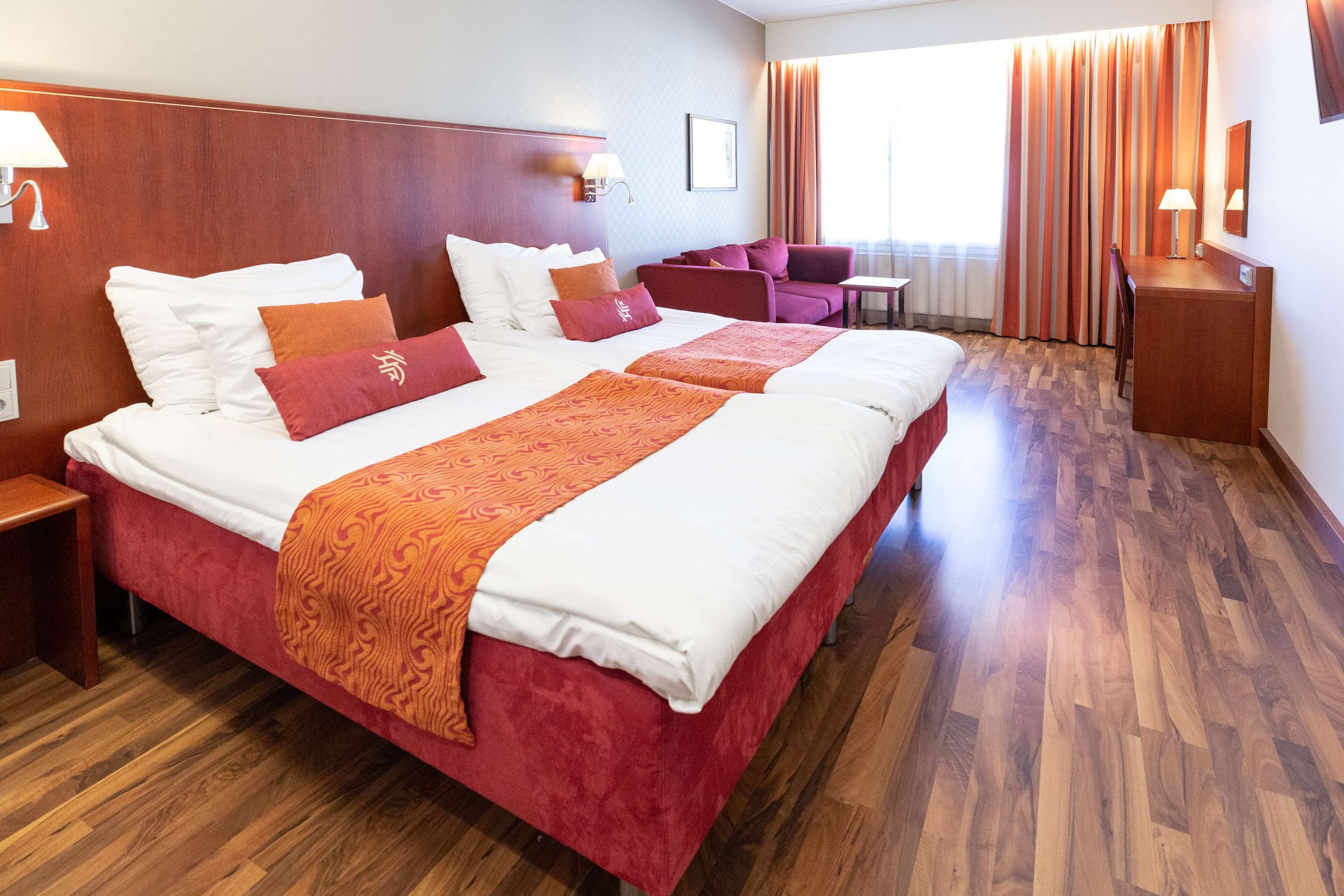 A hotel room with a large bed, a desk, a chair, and a sofa.