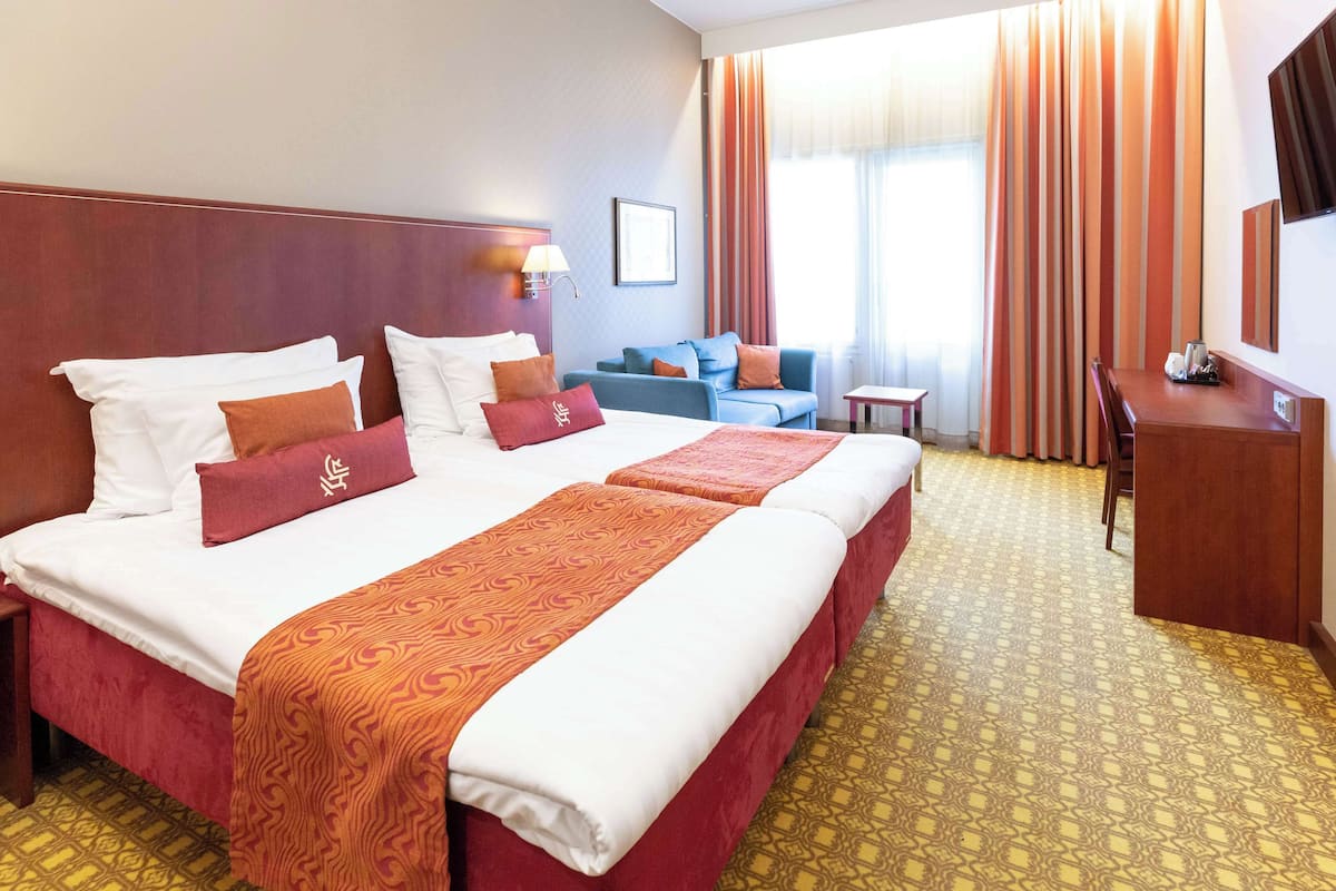 Hotellihuone, jossa on suuri sänky, työpöytä, tuoli, sohva ja televisio.