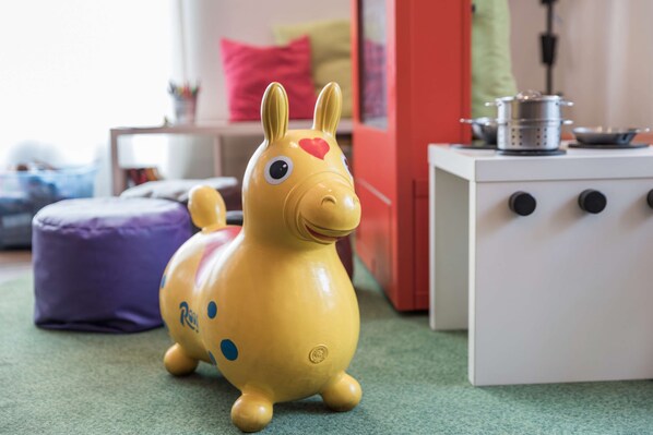 A toy horse on a green carpet with a white cabinet and a purple cushion in the background.