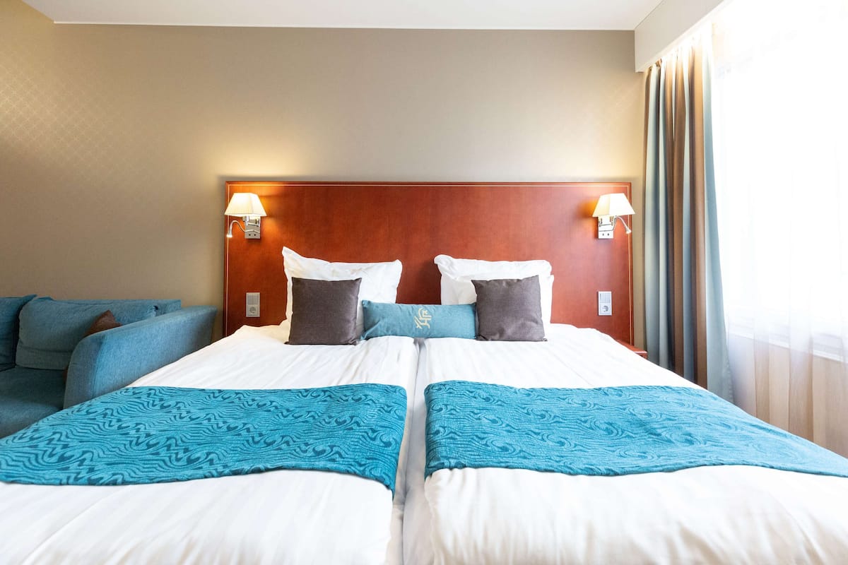 Hotellihuone, jossa on parivuode, kaksi yöpöytää valaisimineen, sängynpääty ja sohva.
