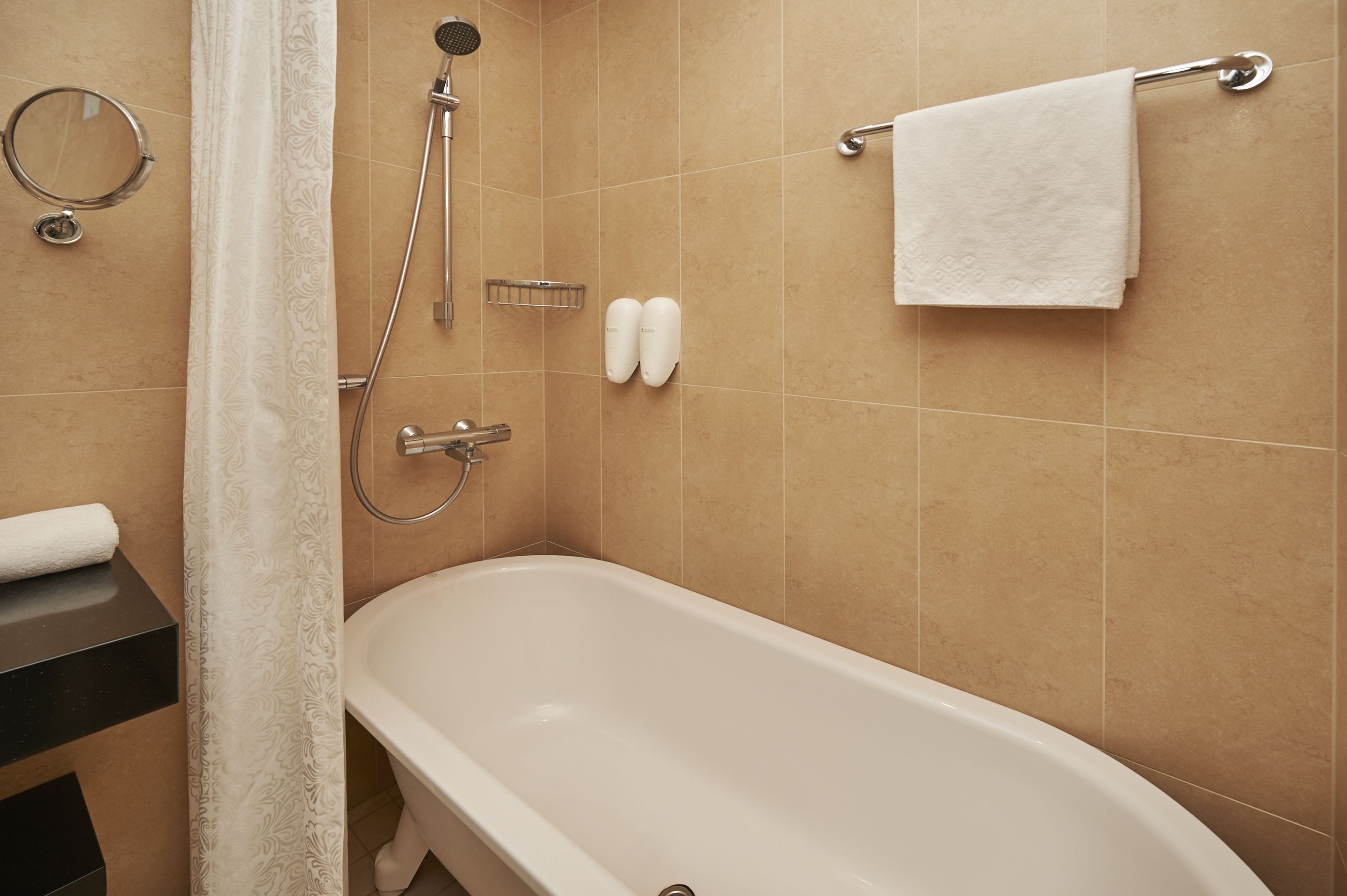 A bathroom with a bathtub, shower, towel rack, and toilet paper dispenser.