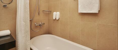 A bathroom with a bathtub, shower, towel rack, and toilet paper dispenser.