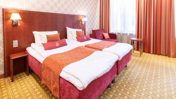 A hotel room with two beds, a wooden headboard, two bedside tables, a small side table, and a patterned carpet.