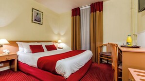 A hotel room with a large bed, a desk with a chair, a lamp, and a bottle of orange juice.