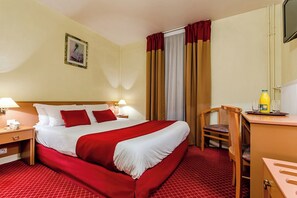 A hotel room with a large bed, a desk with a chair, a lamp, and a bottle of orange juice.