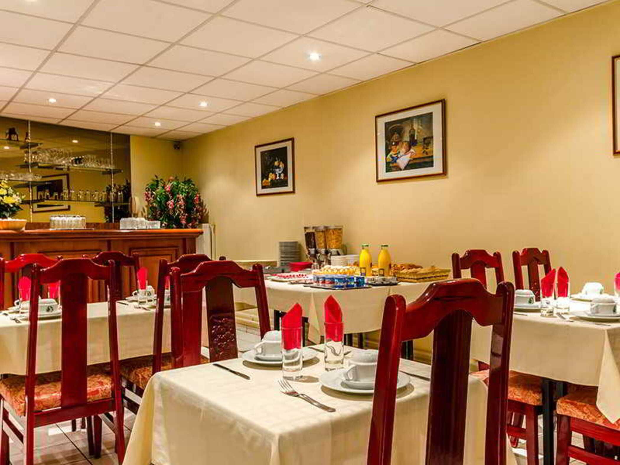 Un espace repas avec des tables préparées pour le petit-déjeuner, où l'on trouve une variété d'aliments et de boissons.