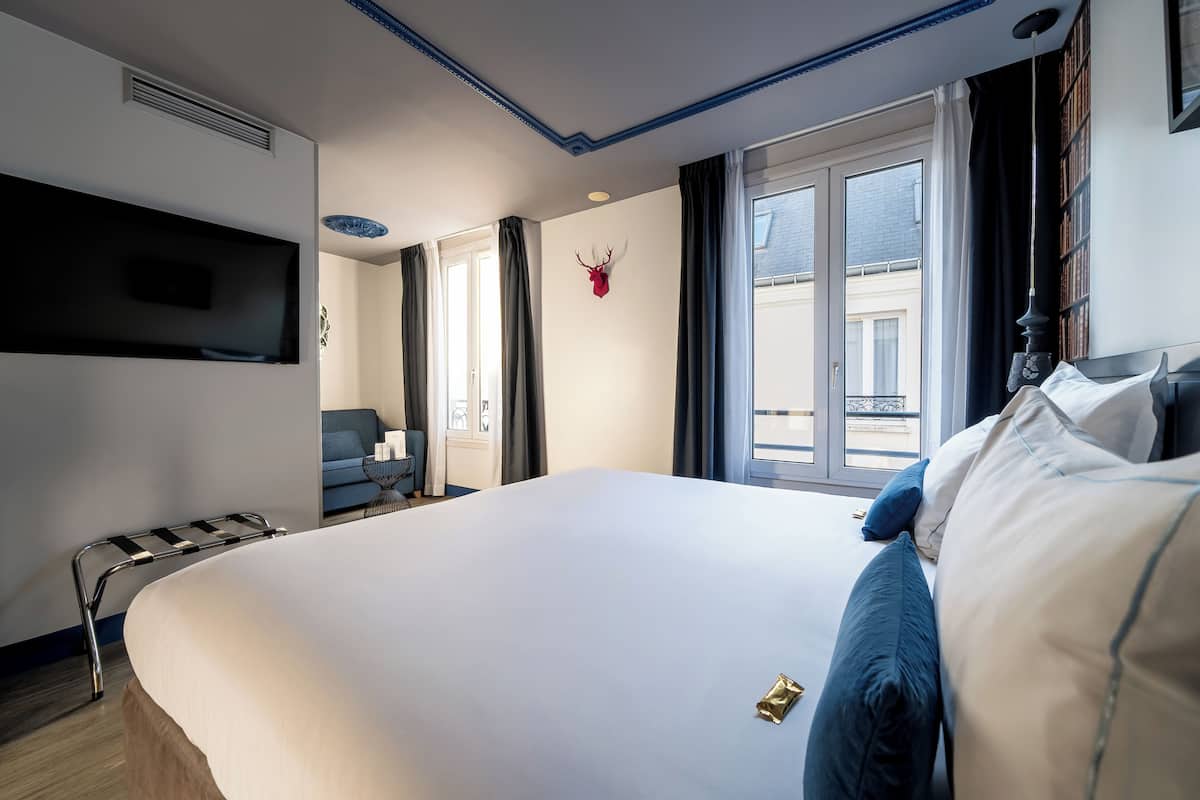 Ett hotellrum med en stor säng, en platt-TV som är monterad på väggen, ett fönster med gardiner och ett uppstoppat rådjurshuvud som hänger på väggen.