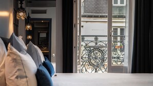 Un dormitorio con cama, almohadas y vistas a un balcón con barandilla de hierro forjado.