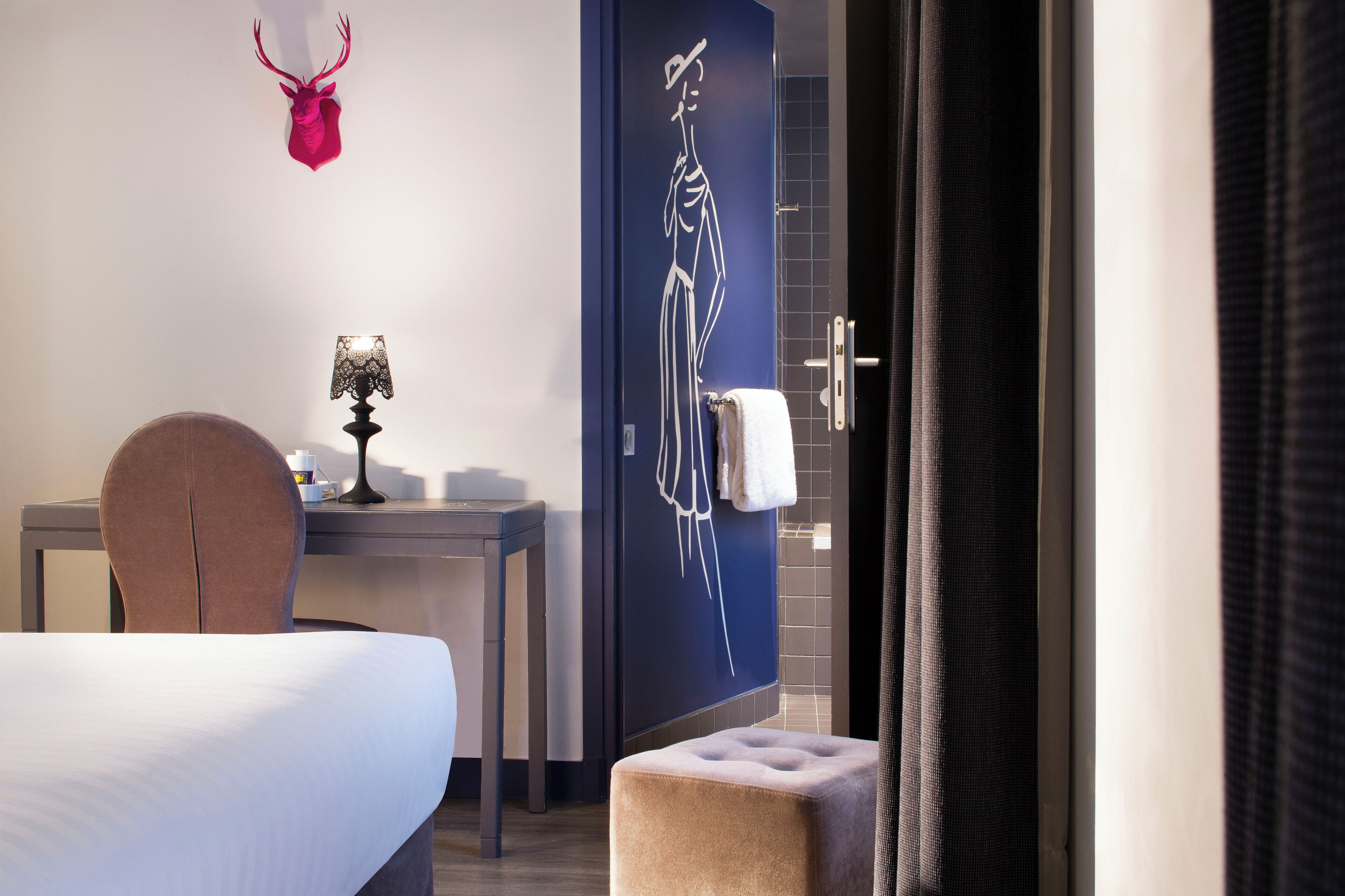 Una habitación de hotel con una cama, un escritorio, una lámpara, un perchero para toallas y un adorno en la pared.