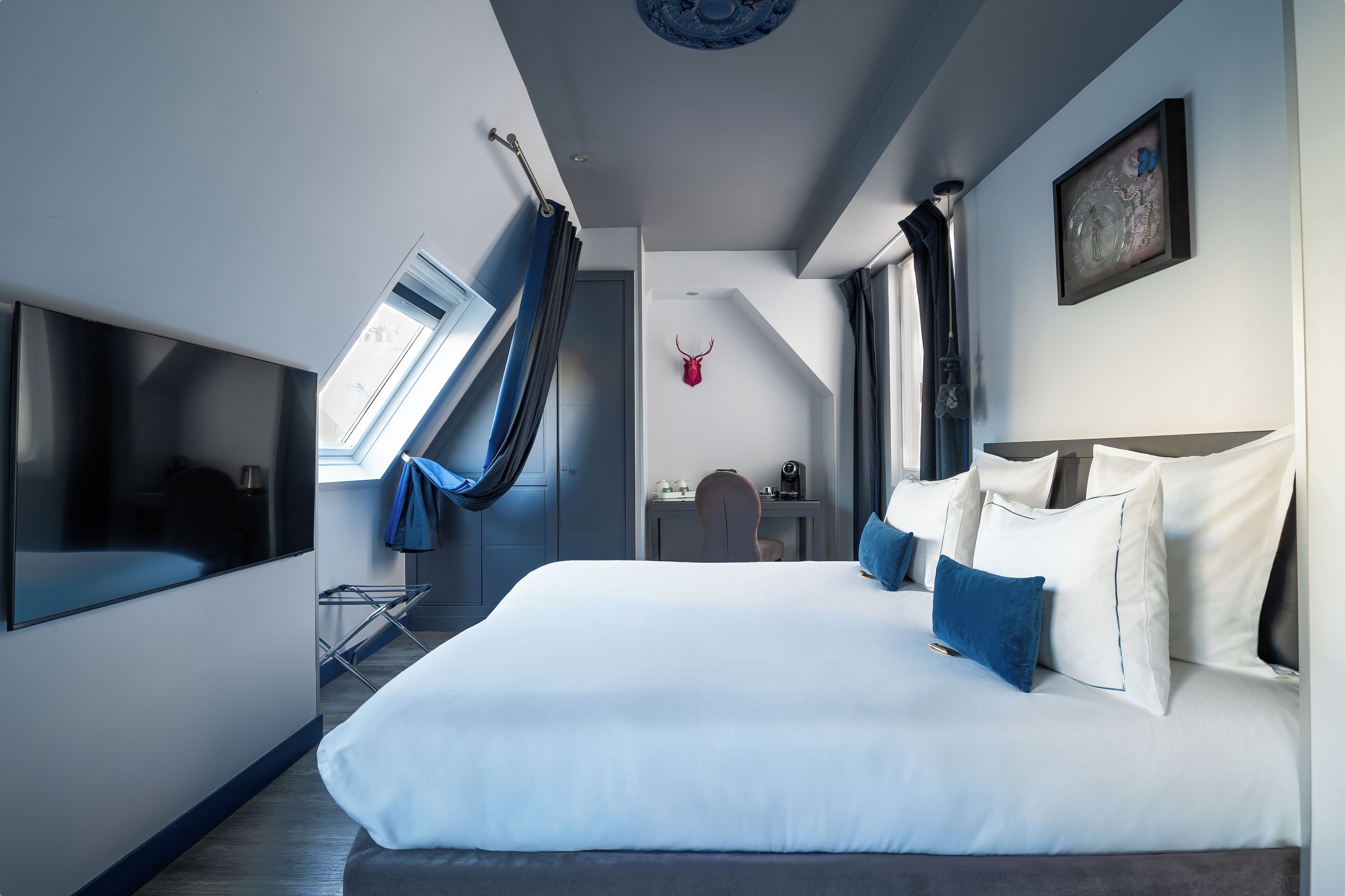 Una habitación de hotel moderna con una cama grande, un escritorio y una silla. Hay una ventana con cortinas, una lámpara en el techo y una obra de arte en la pared.
