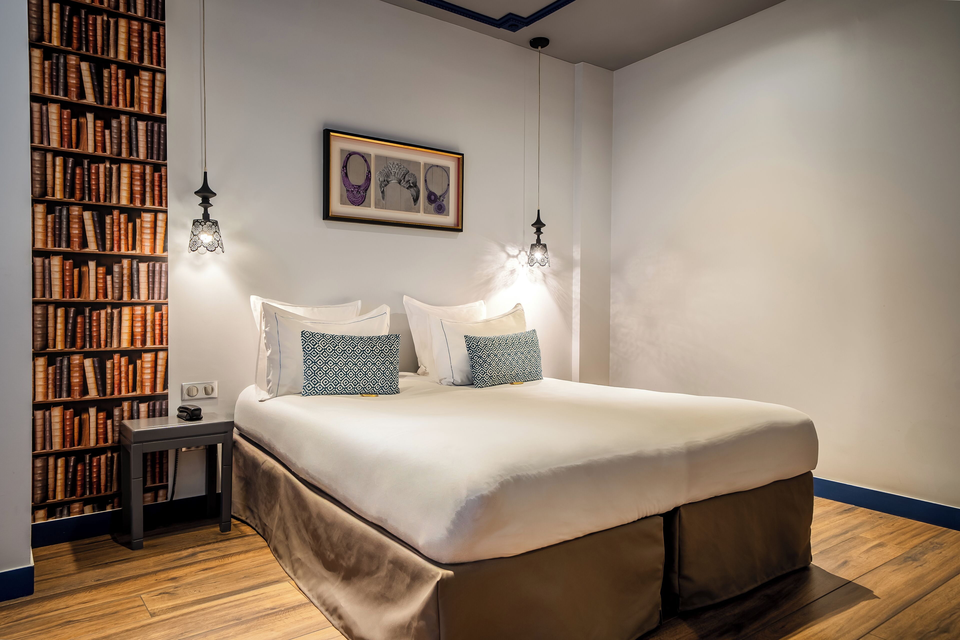 A bedroom with a large bed, two bedside lamps, a nightstand, and a bookshelf filled with books.